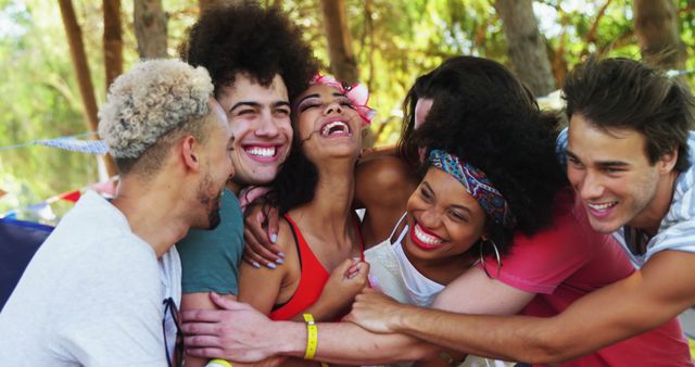 A diverse group of young adults is laughing and embracing at an outdoor gathering, with copy space. Their joyful expressions and casual attire suggest a relaxed and friendly atmosphere at a social event or festival.