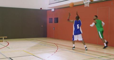 Two african american basketball players shooting and rebounding in indoor gym game