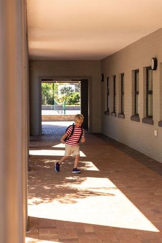Young boy walking through sunlit brick corridor with backpack and striped shirt