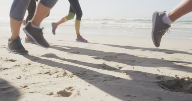 Group of individuals running along sandy beach, showcasing exercise and fitness. Use for health, fitness, lifestyle, and teamwork themes.