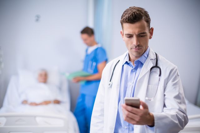 Doctor standing in hospital room using mobile phone, with patient lying in bed and nurse in background. Useful for illustrating modern healthcare, medical technology, communication in healthcare, and hospital environments.