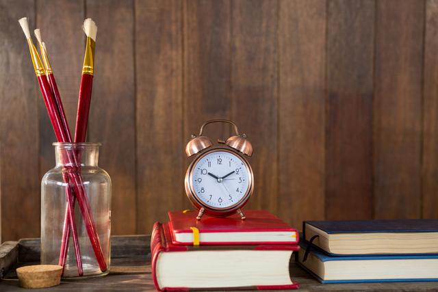 Close-up of books, alarm clock and paint brush arranged on wooden table