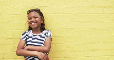 Happy Biracial Girl Smiling by Yellow Wall with Sunglasses