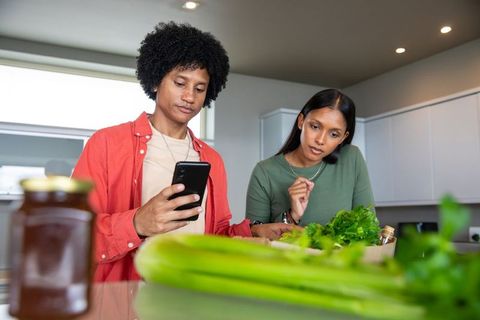 Diverse couple browsing recipes with fresh herbs at kitchen island