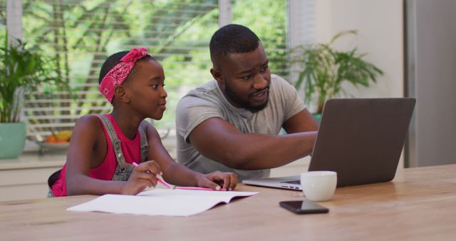 Father assisting his young daughter with her homework in a kitchen setting. Indicates involved parenthood and support for education. Ideal for use in education, family dynamics, parenting articles, online learning resources or advertisements focusing on family activities.