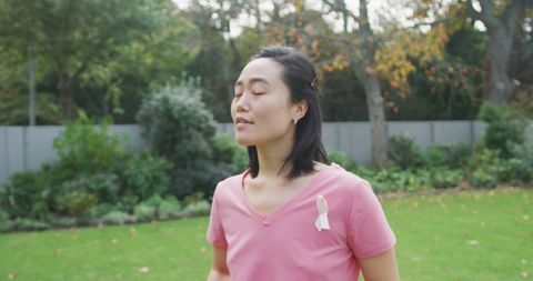 Asian Woman in Pink Shirt with Cancer Awareness Ribbon Relaxing Outdoors