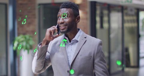 Smiling businessman talking on phone with augmented reality icons in modern lobby