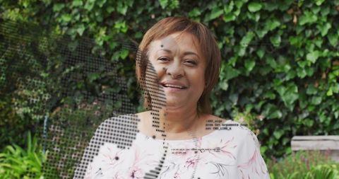 Smiling mature woman standing in backyard wearing pink floral blouse and necklace, serene portrait