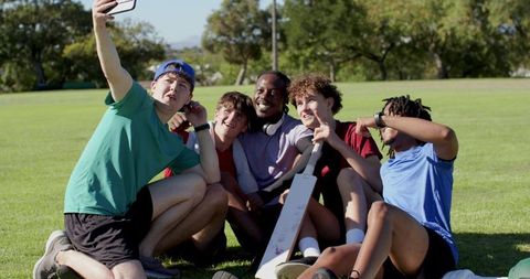 Multiracial friends taking selfie after casual cricket match in sunny park, team bonding
