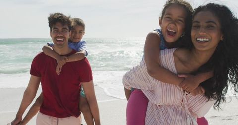 Happy Parents Giving Piggyback Rides to Children on Beach Adventure