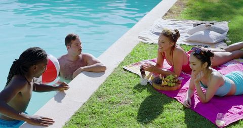 Diverse friends relaxing poolside with beach ball and picnic