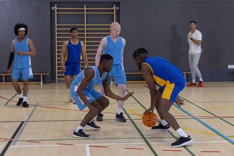 Diverse Male Basketball Players Training Under Coach Indoors