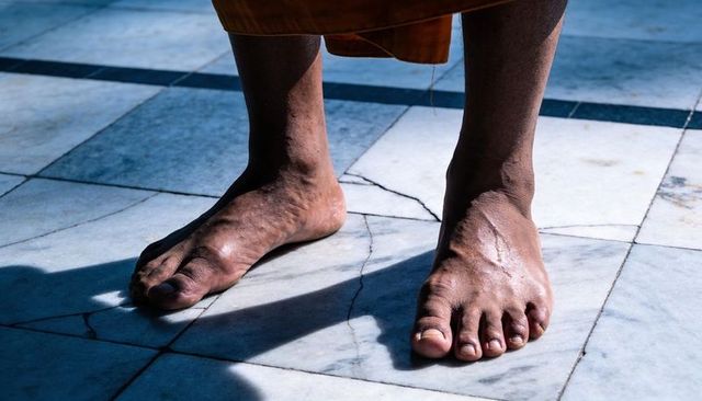 Standing monk bare feet on cracked marble tiles with saffron robe hem