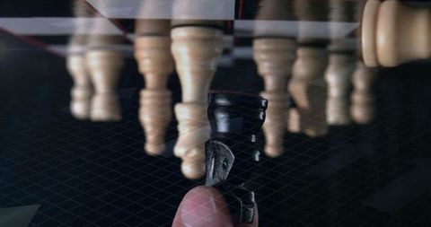 Close-up of hand holding black pawn on reflective chessboard