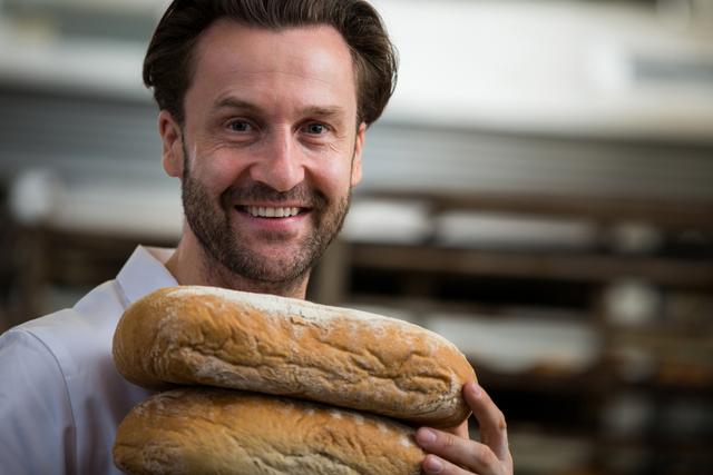 Portrait of smiling baker carrying stack of baked breads