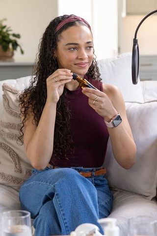 African american influencer livestreaming with amber bottle and mic in cozy natural light home studi