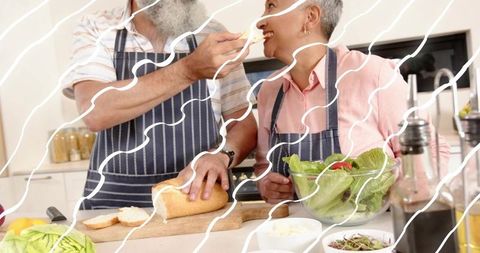 Mature couple sharing playful cooking moment, feeding each other at kitchen counter