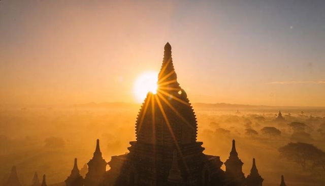 Golden sunrise halo framing ancient pagoda spire over misty plain dawn silhouette