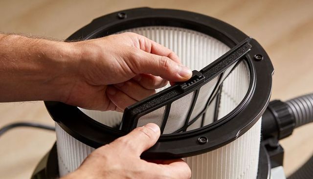 Hands removing prefilter from pleated cartridge vacuum filter for workshop maintenance