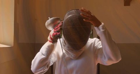 Fencer adjusting mask and foil cord in sunlit minimalist training room