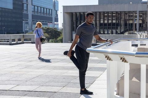 Urban rooftop fitness stretching male athlete at railing with walking commuter in sunlight