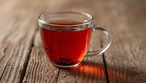 Steeping amber tea in glass cup resting on weathered wood with warm glow