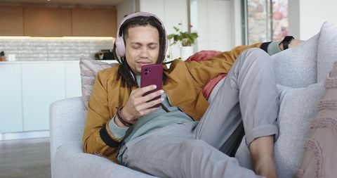 Relaxing man on sofa listening to music and scrolling smartphone in modern living room