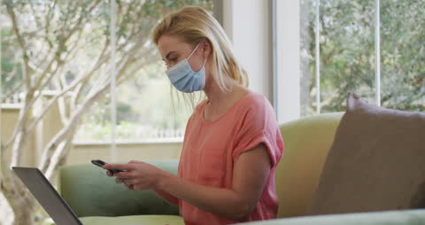 Woman with Face Mask Using Smartphone at Home on Sofa