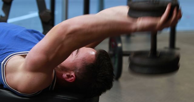 Young man lying on bench focusing on lifting dumbbells in a gym, working on strength training and building muscles. This is suitable for use in fitness articles, gym promotions, health and wellness blogs, and workout guides.