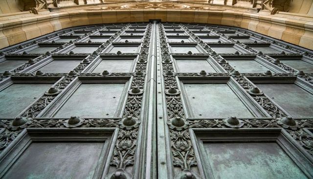 Rising ornate patinated bronze double door with riveted panels and foliate detailing