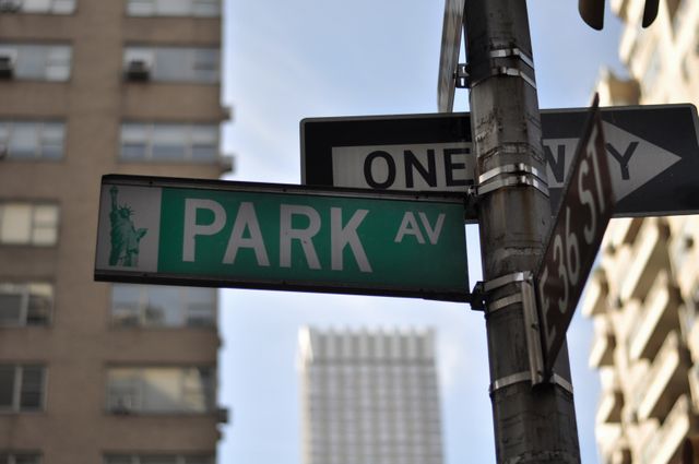 Street sign for Park Avenue photographed against background of tall urban buildings, emphasizing city life. Ideal for illustrating New York City, urban planning, travel guides, or transportation themes. Perfect for use in articles about Manhattan, urban infrastructure, or directions and wayfinding.