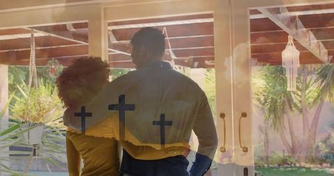 Couple embracing at glass doors with cross reflections and sunlit backyard patio
