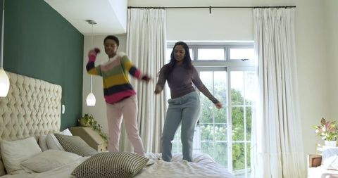 Female Friends Enjoying Fun Moments Jumping on Bed in Modern Bedroom