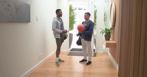 Black and latino men chatting in modern entry hallway holding basketball and gym bags