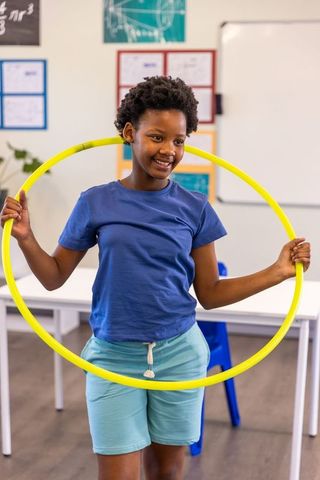 Smiling african american student holding yellow hula hoop in classroom playful activity