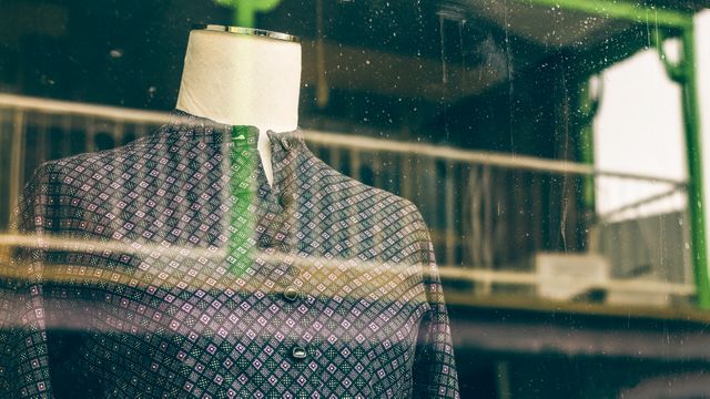 Mannequin dressed in a vintage patterned outfit visible through raindrop-speckled glass, suggesting old-world charm and classic fashion. Suitable for use in promotions for vintage shops, retro clothing lines, and rainy day retail displays. Ideal for illustrating themes of nostalgia and elegant fashion.