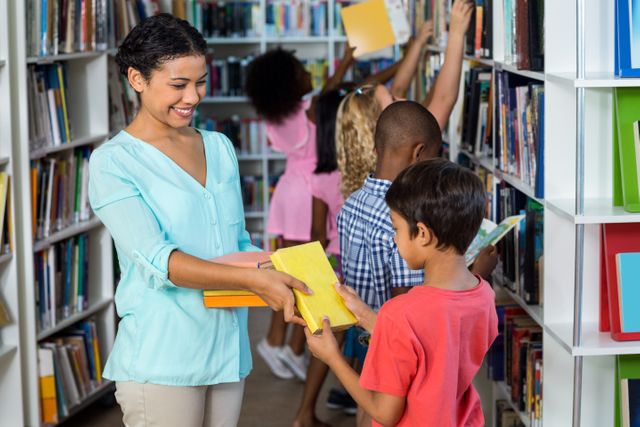 This image shows a smiling female teacher handing books to a young boy in a library, with other children in the background selecting books from shelves. Ideal for use in educational materials, school websites, library promotions, and articles about childhood education and literacy.
