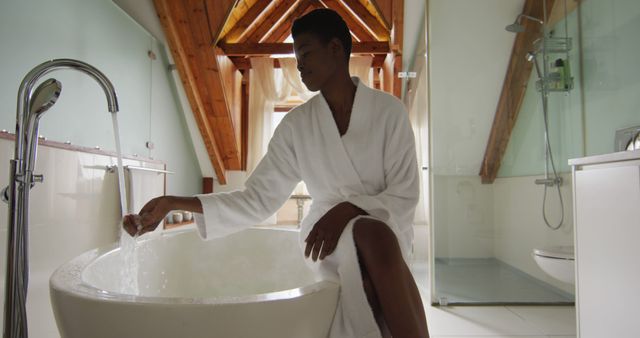 Smiling african american attractive woman in white robe sitting on bathtub, preparing bath. beauty, pampering, home spa and wellbeing concept.