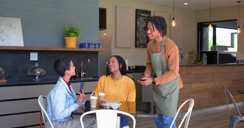 African american barista taking card payment from laughing customers in modern coffeehouse