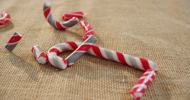 Broken pieces of a red and white candy cane lie scattered on a textured beige surface, with copy space. The shattered candy suggests a holiday treat that has been dropped or playfully crushed.