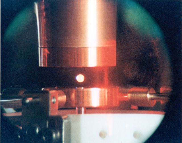 A 3 mm drop of nickel-zirconium, heated to incandescence, hovers between electrically charged plates inside the Electrostatic Levitator (ESL). The ESL uses static electricity to suspend an object (about 2-3 mm in diameter) inside a vacuum chamber while a laser heats the sample until it melts. This lets scientists record a wide range of physical properties without the sample contacting the container or any instruments, conditions that would alter the readings. The Electrostatic Levitator is one of several tools used in NASA's microgravity materials science program. 