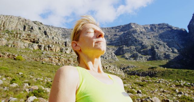 Woman is standing on a rocky mountain trail, basking in sunlight with eyes closed and relaxed expression. Ideal for concepts of mental wellness, outdoor recreation, adventure tourism, nature retreats, and healthy lifestyles.