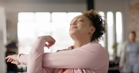 Two women stretching in bright studio wearing pink jacket, wellness and calm