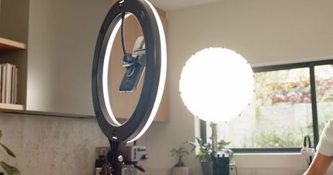 Female creator adjusting ring light and smartphone mount in modern kitchen studio