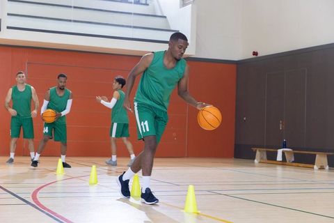 African american player dribbling basketball through cones during team training drill