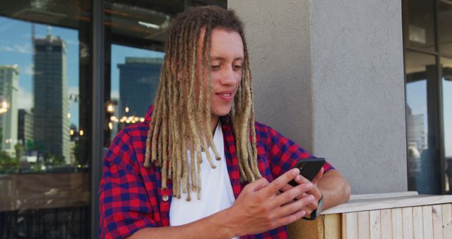 Biracial man with dreadlocks sitting at table outside cafe using smartphone. digital nomad, out and about in the city.