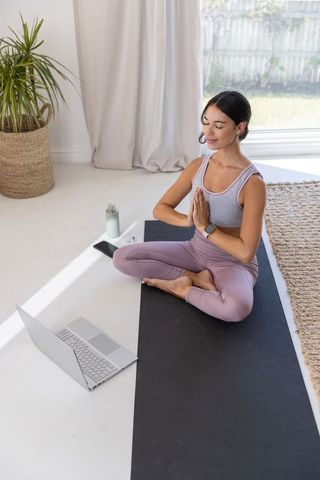 Woman practicing mindful yoga at home with laptop on mat in natural light wellness