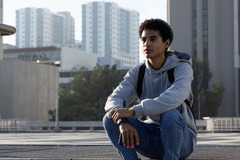 African american teen crouching on rooftop overlooking city skyline holding smartphone