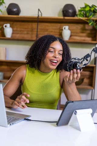 African american woman podcasting speaking into professional microphone at home workspace