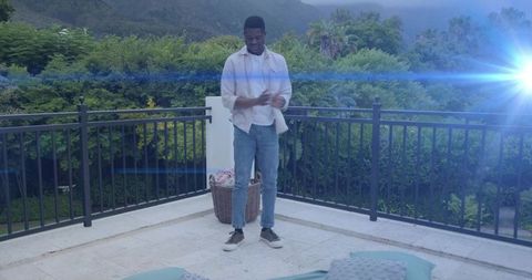 Adjusting shirt sleeves on sunlit terrace with denim casual style and lush greenery